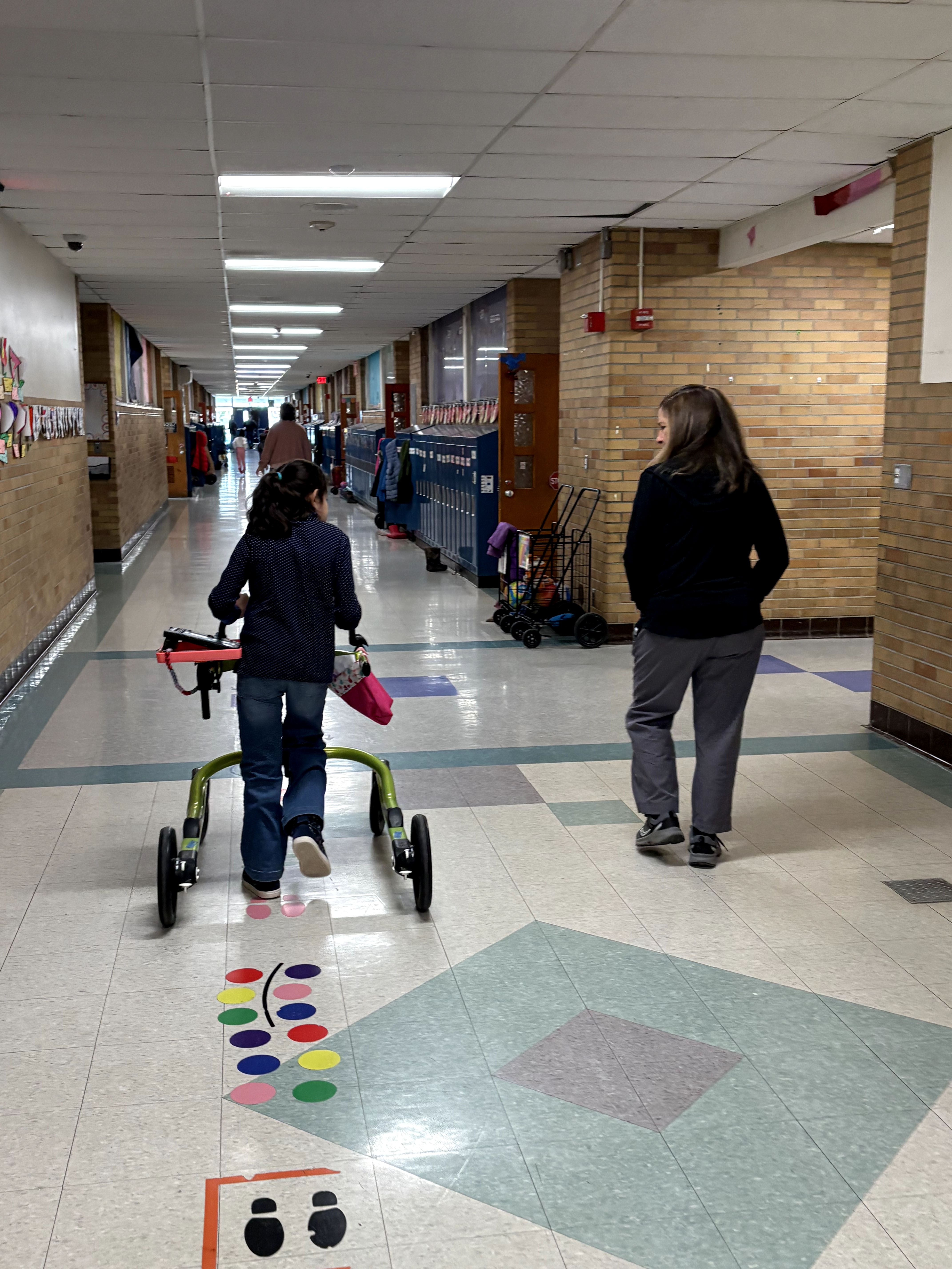 Student walking through a school hallway using the walker with the newest tray prototype attached